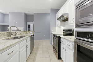 Kitchen with stainless steel appliances, white cabinetry, and light stone countertops