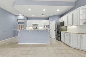 Kitchen featuring light stone countertops, backsplash, white cabinetry, a breakfast bar area, and recessed lighting