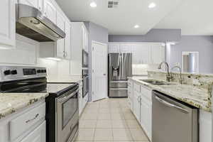 Kitchen with stainless steel appliances, light stone countertops, white cabinetry, light tile patterned floors, and recessed lighting