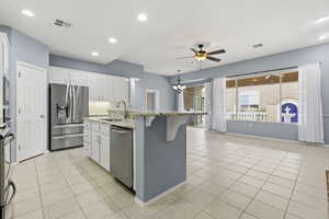 Kitchen with white cabinetry, stainless steel appliances, hanging lights, light stone counters, and a center island with sink