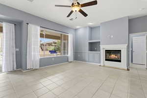 Unfurnished living room featuring a ceiling fan, built in features, light tile patterned floors, and a glass covered fireplace