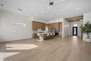 Kitchen featuring a breakfast bar, light countertops, an island with sink, open floor plan, and a ceiling fan