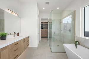 Bathroom with a spacious closet, tiled shower, double vanity, a freestanding tub, and recessed lighting