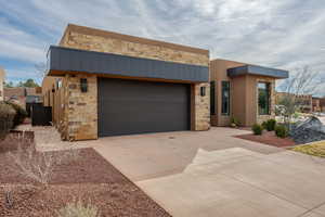 Modern home with stone siding, driveway, stucco siding, and an attached garage