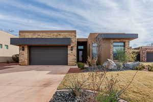 Modern home with stone siding, driveway, an attached garage, and stucco siding