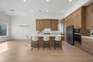Kitchen featuring a breakfast bar, hanging light fixtures, a kitchen island with sink, stainless steel appliances, and light wood finished floors