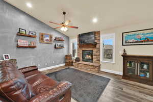 Living room featuring vaulted ceiling, recessed lighting, wood finished floors, ceiling fan, and a stone fireplace