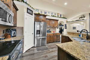 Kitchen with stainless steel appliances, arched walkways, light wood-style flooring, backsplash, and light stone countertops