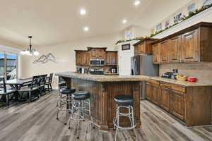Kitchen with tasteful backsplash, a kitchen breakfast bar, lofted ceiling, an island with sink, and light stone counters