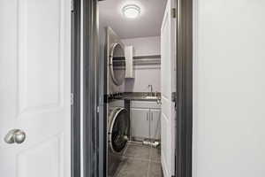 Laundry room featuring stacked washer and dryer, dark tile patterned flooring, and cabinet space
