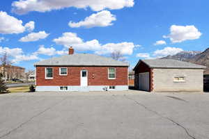 View of property exterior featuring an outdoor structure, brick siding, a chimney, a garage, and a mountain view