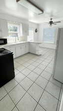 Kitchen featuring white cabinetry, black appliances, decorative backsplash, light tile patterned floors, and a peninsula