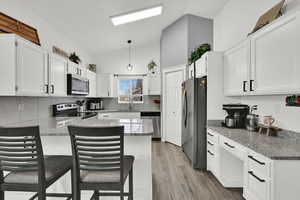 Kitchen with lofted ceiling, white cabinets, light stone countertops, and pendant lighting