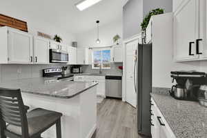 Kitchen featuring lofted ceiling, light stone counters, a peninsula, white cabinetry, and hanging light fixtures