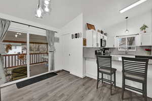 Kitchen with decorative light fixtures, white cabinets, light stone countertops, vaulted ceiling, and tasteful backsplash