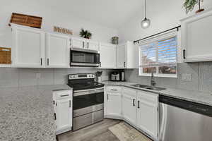 Kitchen with stainless steel appliances, light stone counters, white cabinetry, pendant lighting, and light wood finished floors