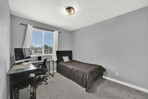 Carpeted bedroom featuring an office area and a textured ceiling