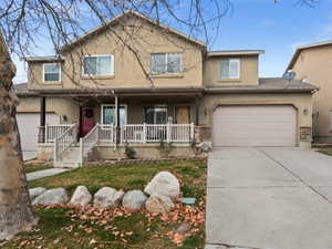 Traditional-style home with stucco siding, covered porch, concrete driveway, an attached garage, and a front yard