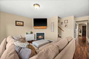 Living area with arched walkways, a glass covered fireplace, and dark wood finished floors