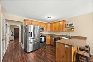 Kitchen with stainless steel appliances, arched walkways, open shelves, a peninsula, and a kitchen breakfast bar