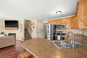 Kitchen featuring stainless steel appliances, a peninsula, a glass covered fireplace, a kitchen breakfast bar, and dark wood finished floors