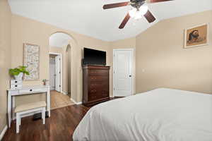 Bedroom featuring arched walkways, lofted ceiling, dark wood finished floors, and ceiling fan