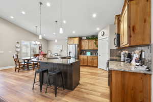 Dual tone kitchen with stainless steel appliances, a center island with sink, dark stone counters, a kitchen breakfast bar, and light wood finished floors