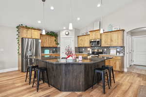 Kitchen with a kitchen bar, stainless steel appliances, arched walkways, dark stone counters, and lofted ceiling