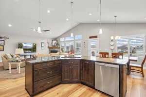 Kitchen featuring dark wood finish cabinetry, a kitchen island with sink, open floor plan, stainless steel dishwasher, and dark stone counters