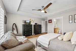Bedroom with a tray ceiling, ceiling fan, wood finished floors, and connected bathroom