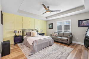 Bedroom featuring a tray ceiling, light wood-style floors, a ceiling fan, and a decorative wall