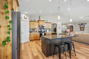 Kitchen featuring arched walkways, dark stone countertops, open floor plan, a kitchen breakfast bar, and stainless steel appliances