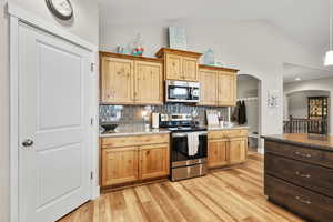 Kitchen featuring stainless steel appliances, light stone countertops, arched walkways, light wood-style flooring, and vaulted ceiling