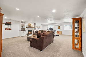 Living area with a stone fireplace, light carpet, a textured ceiling, built in shelves, and recessed lighting