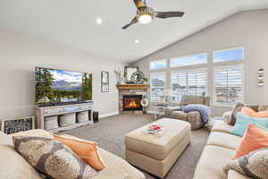 Carpeted living room with a tiled fireplace, vaulted ceiling, a ceiling fan, and recessed lighting