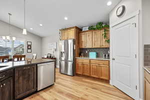 Kitchen featuring stainless steel appliances, dark stone countertops, light wood-style floors, lofted ceiling, and backsplash