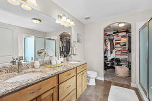 Bathroom with a walk in closet, a shower stall, double vanity, and wood finish floors