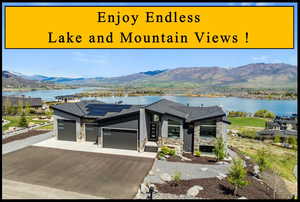 View of front of home featuring stone siding, a garage, solar panels, a water and mountain view, and asphalt driveway