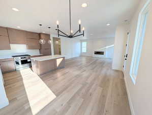 Kitchen featuring gas stove, a kitchen island, light wood finished floors, open floor plan, and suspended lighting