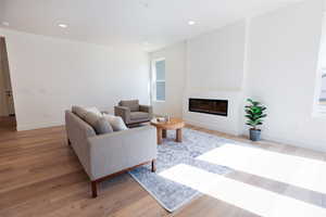 Living room featuring light wood finished floors, a glass covered fireplace, and recessed lighting