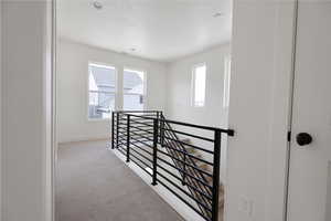 Hallway with light colored carpet and an upstairs landing
