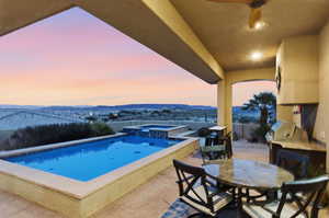 Pool at dusk featuring a patio area, a pool with connected hot tub, a mountain view, and an outdoor kitchen / dining area