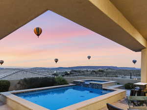 Pool at dusk featuring a mountain view, a pool with connected hot tub, and a patio