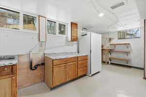 Kitchen with wood finish cabinets, concrete flooring, and freestanding refrigerator