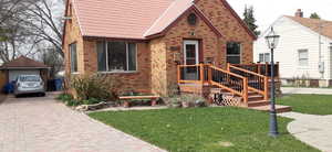 View of front of house with a front lawn, brick siding, a wooden deck, and decorative driveway