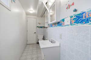 Bathroom featuring vanity, light flooring, tile walls, and a wainscoted wall