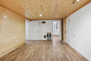 Unfurnished living room featuring wood ceiling, wood finished floors, heating unit, and wood walls