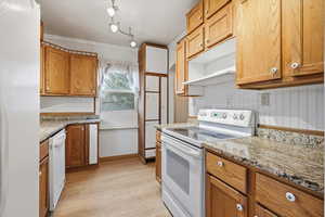 Kitchen with white appliances, wood finish cabinetry, light wood-style flooring, light stone countertops, and ornamental molding