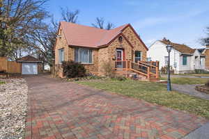 View of front of home featuring an outdoor structure, brick siding, decorative driveway, a detached garage, and a front yard
