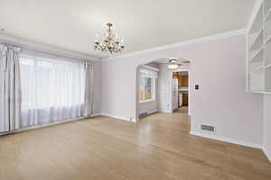 Empty room with arched walkways, light wood-style floors, suspended lighting, and a ceiling fan